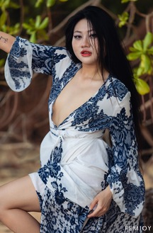 May Poses Nude Under Palm Trees In Tropical Heat, Black Hair Flowing As She Leans Against Bark